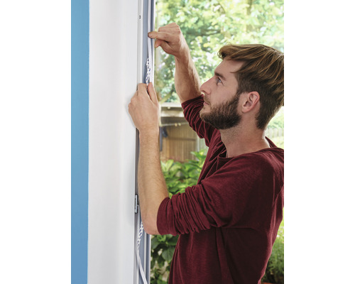 Mann befestigt Dichtungsband an einem Fensterrahmen zur Isolierung.