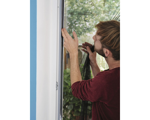 Mann befestigt ein Insektenschutzgitter an einem Fensterrahmen.