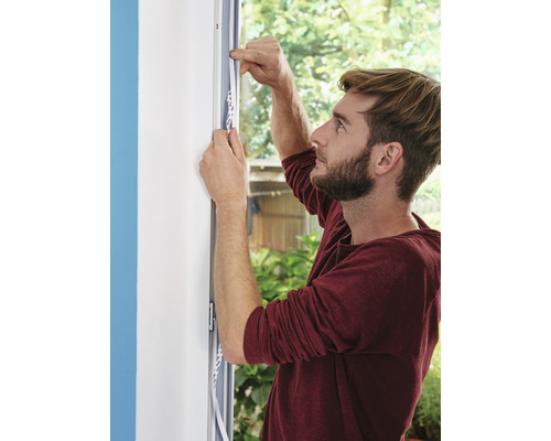 Un homme fixe une bande d''étanchéité sur un cadre de fenêtre.