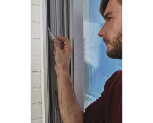 Un homme installe une moustiquaire à la fenêtre