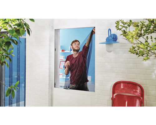 Un homme fixe une moustiquaire sur une fenêtre pour empêcher les insectes d''entrer