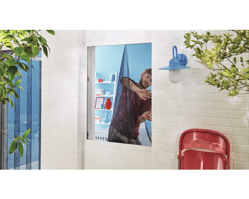 Un homme installe une moustiquaire sur une fenêtre pour se protéger des insectes.