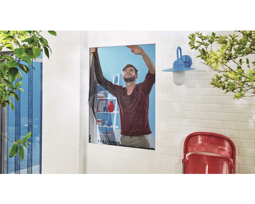 Un homme installe une moustiquaire sur une fenêtre pour empêcher les insectes d''entrer.