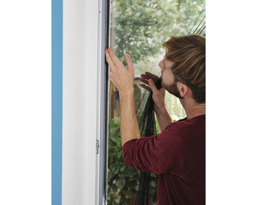 Un homme fixe une moustiquaire sur le cadre de la fenêtre pour se protéger des insectes.