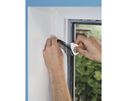 Une personne fixe un écran anti-insectes sur un cadre de fenêtre à l''aide d''un outil de montage.