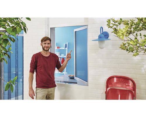 Un homme se tient devant une fenêtre avec une moustiquaire et la montre du doigt.
