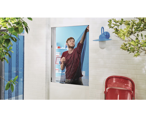 Un homme installe une moustiquaire devant une fenêtre.