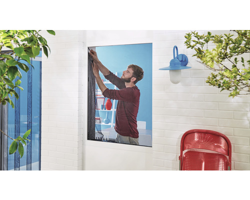 Un homme fixe une moustiquaire à une fenêtre.