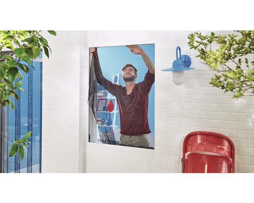 Un homme installe une moustiquaire sur une fenêtre pour empêcher les insectes d''entrer.