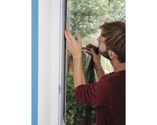 Mann befestigt ein Insektenschutzgitter an einem Fensterrahmen.