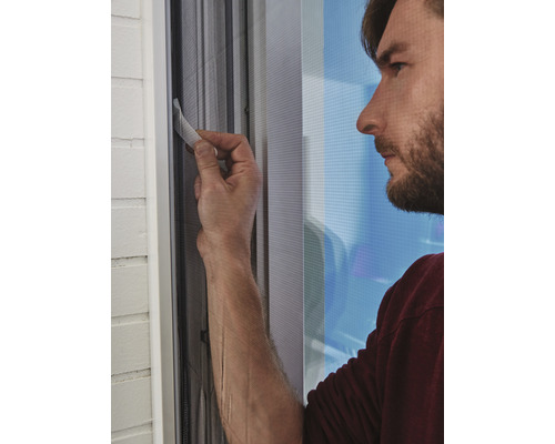 Ein Mann befestigt ein Fliegengitter an einem Fenster.