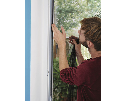 Un homme fixe une moustiquaire sur un cadre de fenêtre.