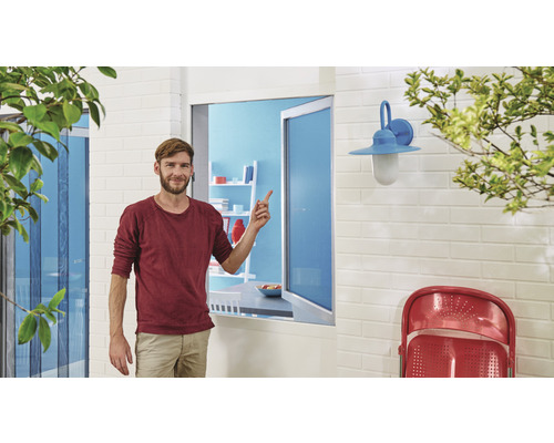 Un homme se tient devant une fenêtre avec moustiquaire, une applique murale extérieure et des meubles de jardin