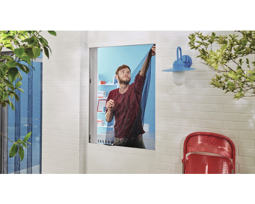 Un homme fixe une moustiquaire à une fenêtre.