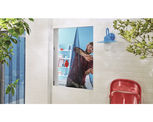 Un homme installe une moustiquaire sur une fenêtre.