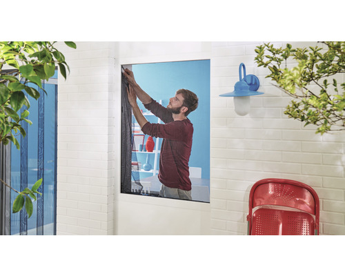 Un homme installe une moustiquaire sur une fenêtre.