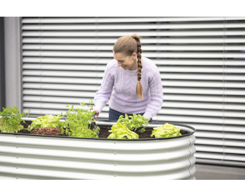Eine Frau arbeitet in einem Hochbeet mit Salat und Kräutern.