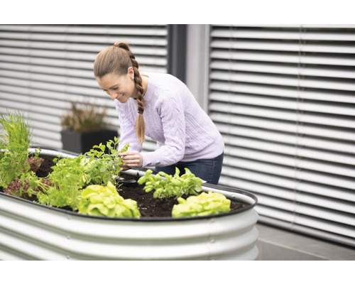 Frau gärtnert in einem Hochbeet mit Gemüse und Kräutern auf einer Terrasse.