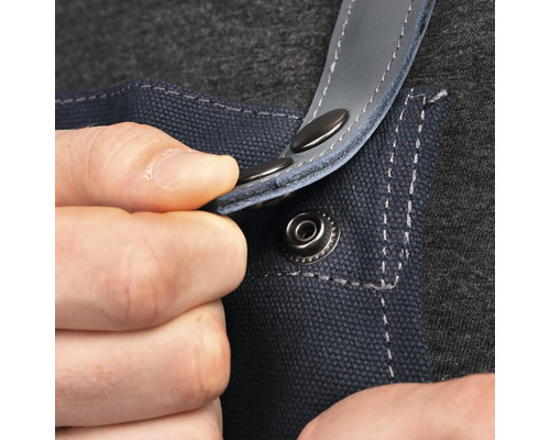 Detailaufnahme einer Person, die einen Druckknopf an einer blauen Arbeitsschürze befestigt.