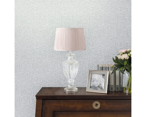 Dekorative Tapete mit Blattmuster, kombiniert mit Lampe, Bilderrahmen, Büchern und Blumenstrauß auf einem Tisch