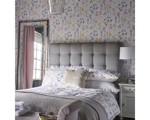 Chambre lumineuse avec papier peint à motifs floraux, tête de lit rembourrée et miroir