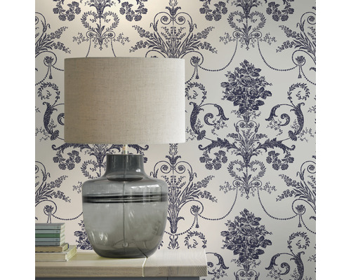 Pièce décorative avec une lampe de table devant un papier peint à motifs floraux.