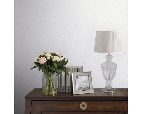 Dekorative Tapete mit zartem Muster in einem Interieur mit Blumen, Büchern und einer Lampe auf einem Holzschreibtisch.