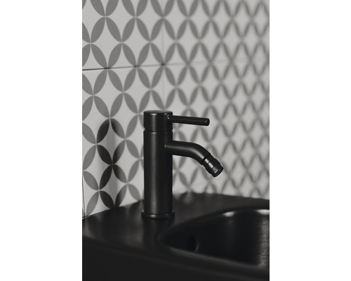 Robinet de lavabo noir sur un lavabo devant un mur de carreaux à motifs