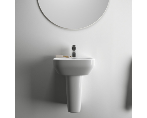 Lavabo avec colonne, robinet, savon et miroir dans une salle de bains claire.