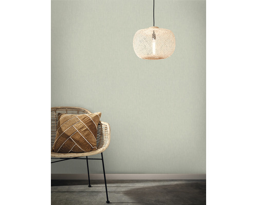 Raumansicht mit Rattansessel, Dekokissen und Rattanlampe vor einer strukturierten Wandtapete.