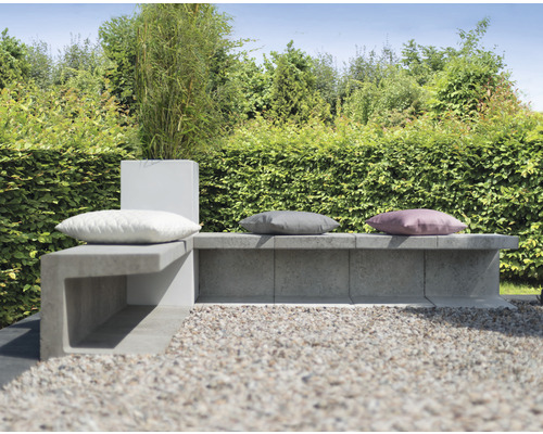 Ensemble de sièges de jardin avec banc en béton et coussins devant une haie verte
