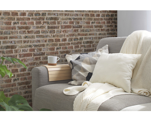 Salon avec canapé, coussins, couverture et mur aspect brique