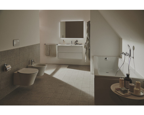 Helles Badezimmer mit Toilette, Bidet, Waschtisch, beleuchtetem Spiegel und Badewanne.