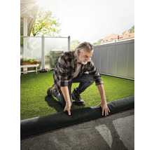 Un homme pose du gazon synthétique sur une terrasse.