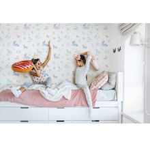 Zwei Mädchen spielen auf einem Bett vor einer Tapete mit Einhornmuster.