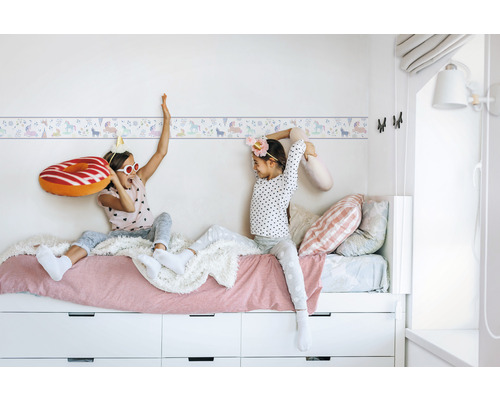 Kinderzimmer mit Einhornbordüre und spielenden Kindern auf einem Bett mit Schubladen