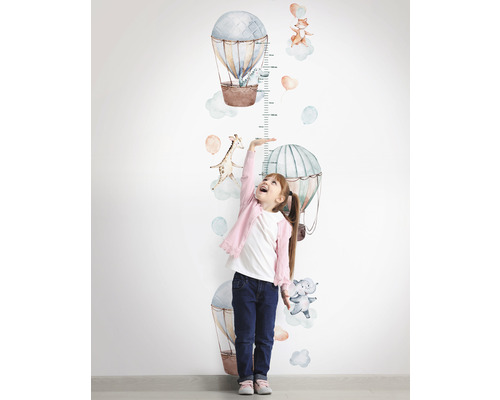 Mädchen misst ihre Größe mit einer Wandtattoo-Messlatte mit Heißluftballon- und Tiermotiven
