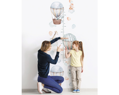 Mutter misst die Größe eines Kindes mit einer Wandtattoo-Messlatte mit Heißluftballon- und Tiermotiven.