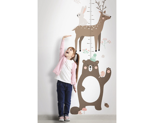 Une fille mesure sa taille à côté d''un mètre autocollant mural avec des motifs d''animaux forestiers.