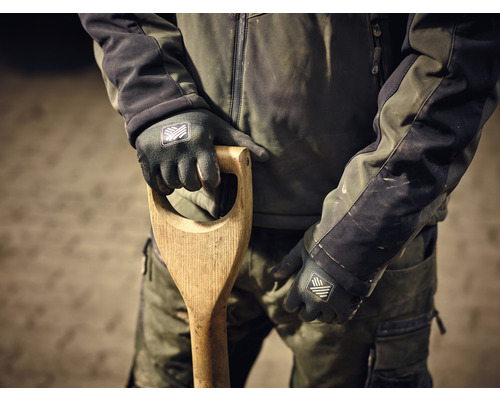 Une personne en vêtements de travail tient une bêche avec un manche en bois et porte des gants de travail.