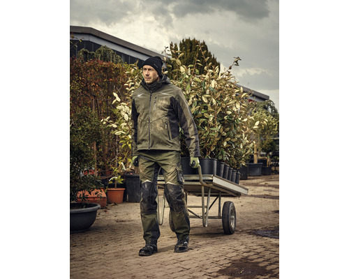 Homme en vêtements de travail poussant une brouette remplie de plantes