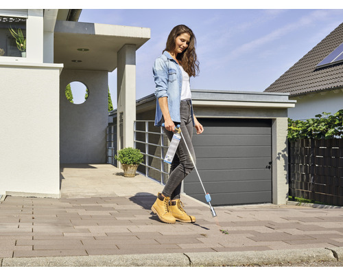 Une femme enlève les mauvaises herbes avec un désherbeur devant une maison.