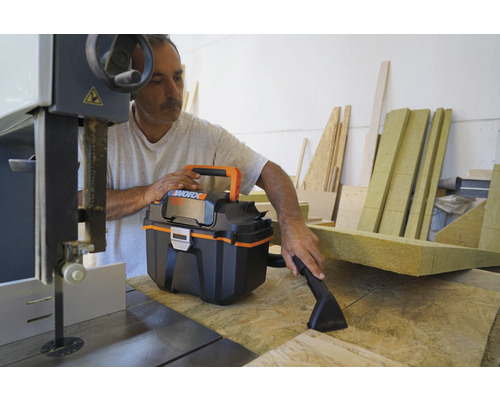 Artisan utilisant un aspirateur eau et poussière sur un établi avec une scie à ruban et des restes de bois
