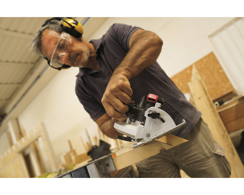 Un homme scie une planche de bois avec une mini-scie circulaire portative tout en portant des lunettes de protection et un casque antibruit.