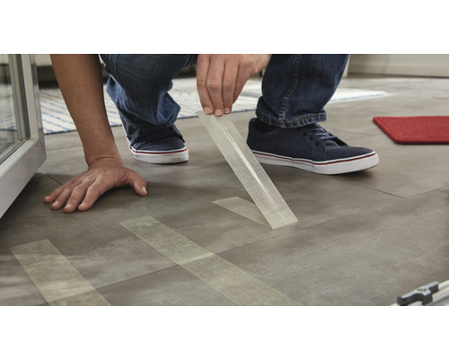 Un homme pose des carreaux avec du ruban adhésif pour la fixation