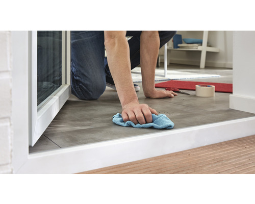 Une personne essuie le sol avec un chiffon près d''une fenêtre.