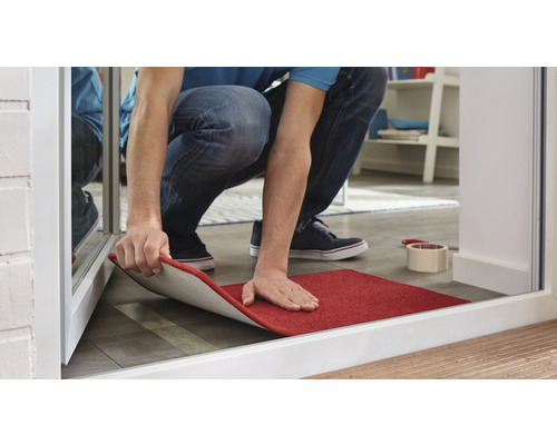 Une personne installe un paillasson rouge à l''intérieur