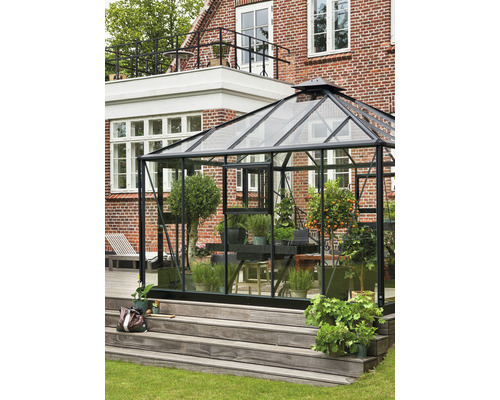 Serre avec plantes sur une terrasse en bois devant une maison en briques.