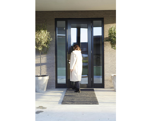 Une femme entre dans une maison avec une porte d''entrée, un paillasson et des bacs à plantes.