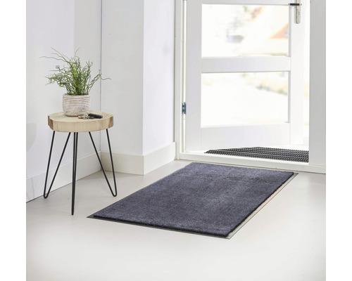 Graue Fußmatte vor einer offenen Tür und einem Beistelltisch mit einer Pflanze